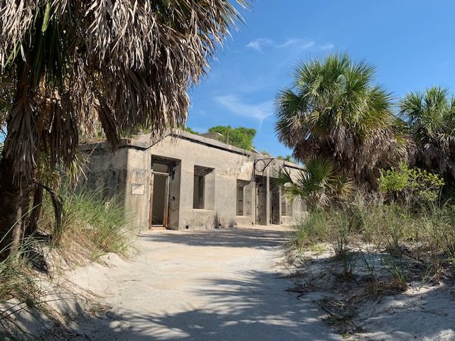 A path leads to an old building in the sand.