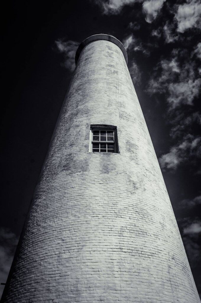 Monochrome image of a tall lighthouse against a cloudy sky, captured from a low angle near Treasure Island.