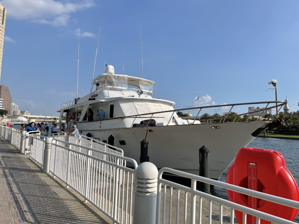 A luxury yacht docked at a city pier on a sunny day with pedestrians nearby, offering exclusive boat tours around Tampa Bay.