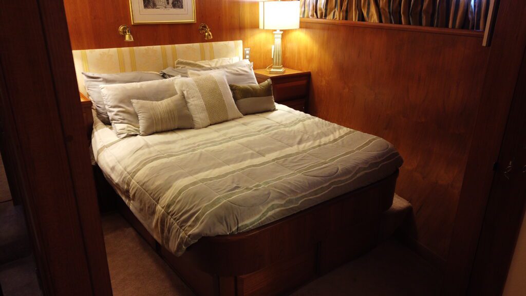 A neatly made bed with white bedding in a warmly lit bedroom with wooden decor, reminiscent of those found on luxury yacht charters in Tampa.