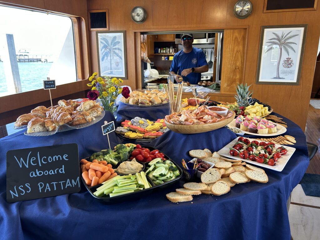 A spread of gourmet food on a boat with a "welcome aboard nss pattam" sign.