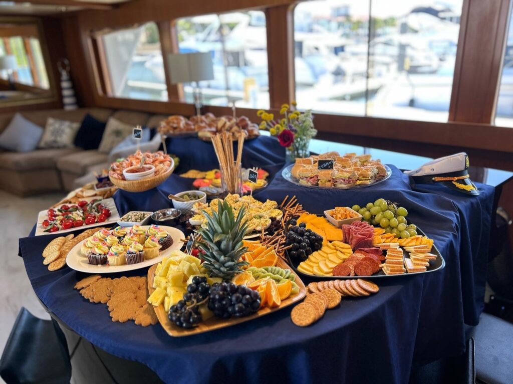 A lavish spread of appetizers and snacks arranged on a table inside a well-appointed yacht cabin.