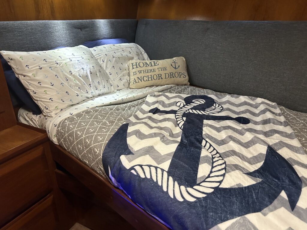 A neatly made bed with nautical-themed bedding and a decorative pillow that reads "home is where the anchor drops" on a yacht charter in Tampa.